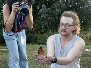 A Monarch butterfly rests on the hands of a community participant as a photojournalist takes photos of the moment.
